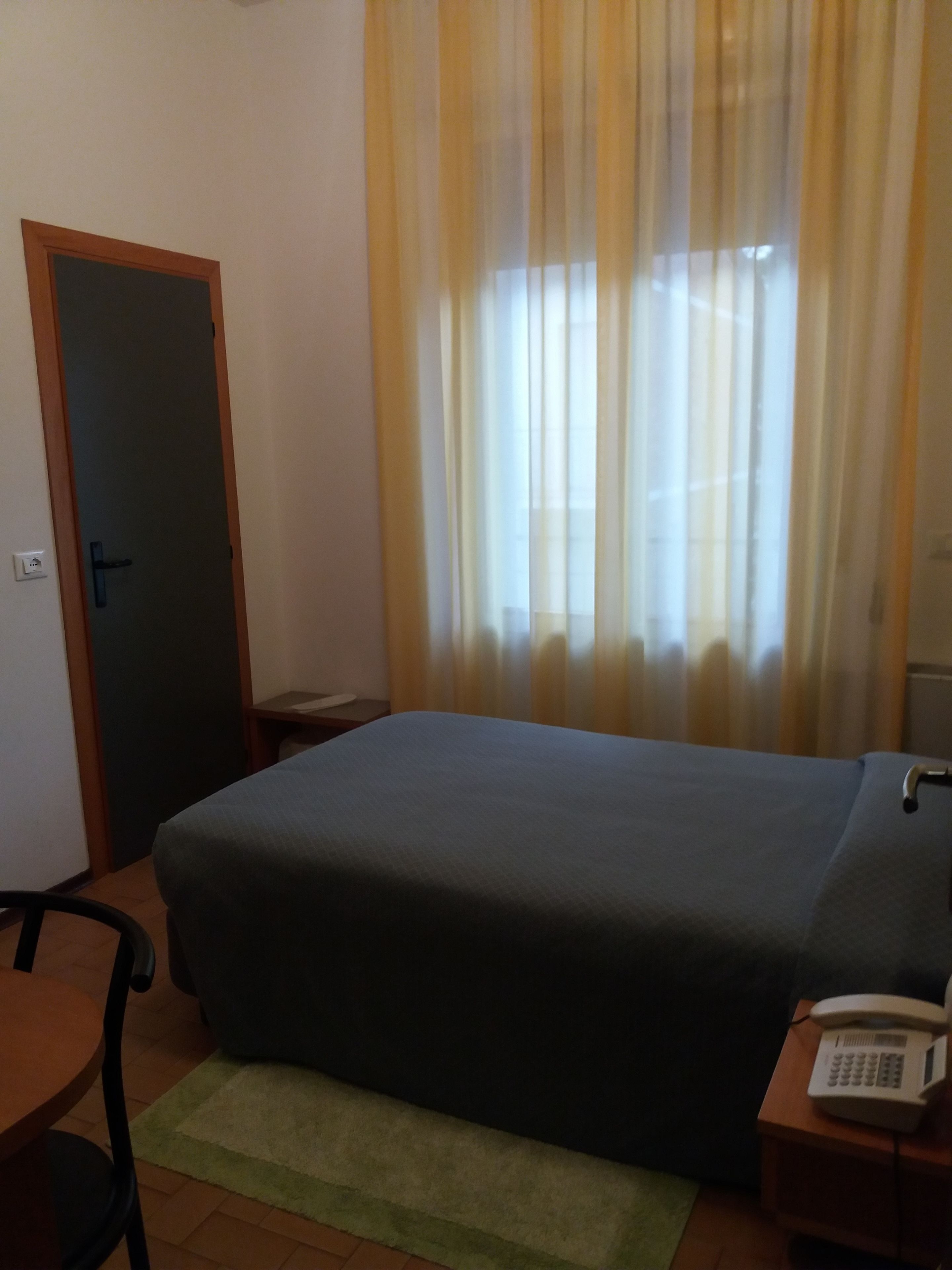 Ein Hotelzimmer mit Bett, Schreibtisch, Stuhl, Telefon und einem Fenster mit Vorhängen.