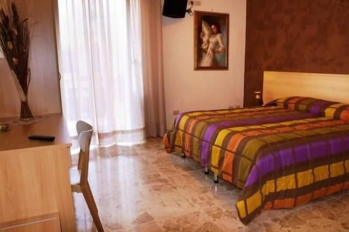 A bedroom with a bed, a desk, a chair, and a painting on the wall.
