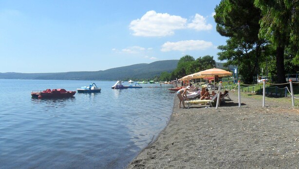 A lakeside beach with boats, umbrellas, and people relaxing. - B&B Raggio di Sole (Trevignano Romano)