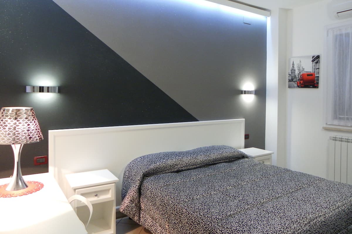 A bedroom with a bed, bedside table, lamp, and wall-mounted light fixtures.