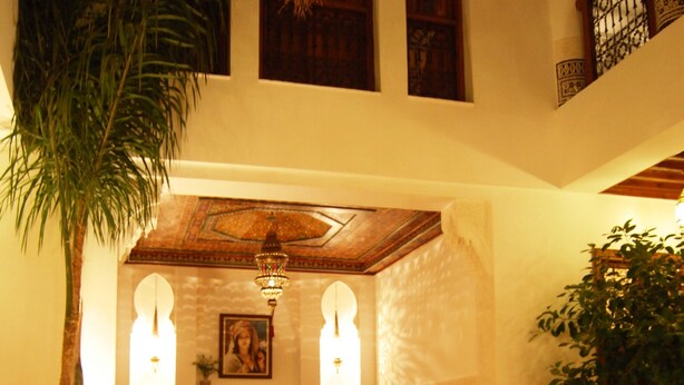 A traditional Moroccan interior with a seating area, a decorative fountain, and a large plant.