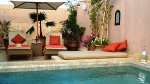 A pool area with lounge chairs, a small table, and potted plants.