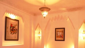 A well-lit bedroom with a large bed, a small table with a vase, and two wall-mounted lamps.