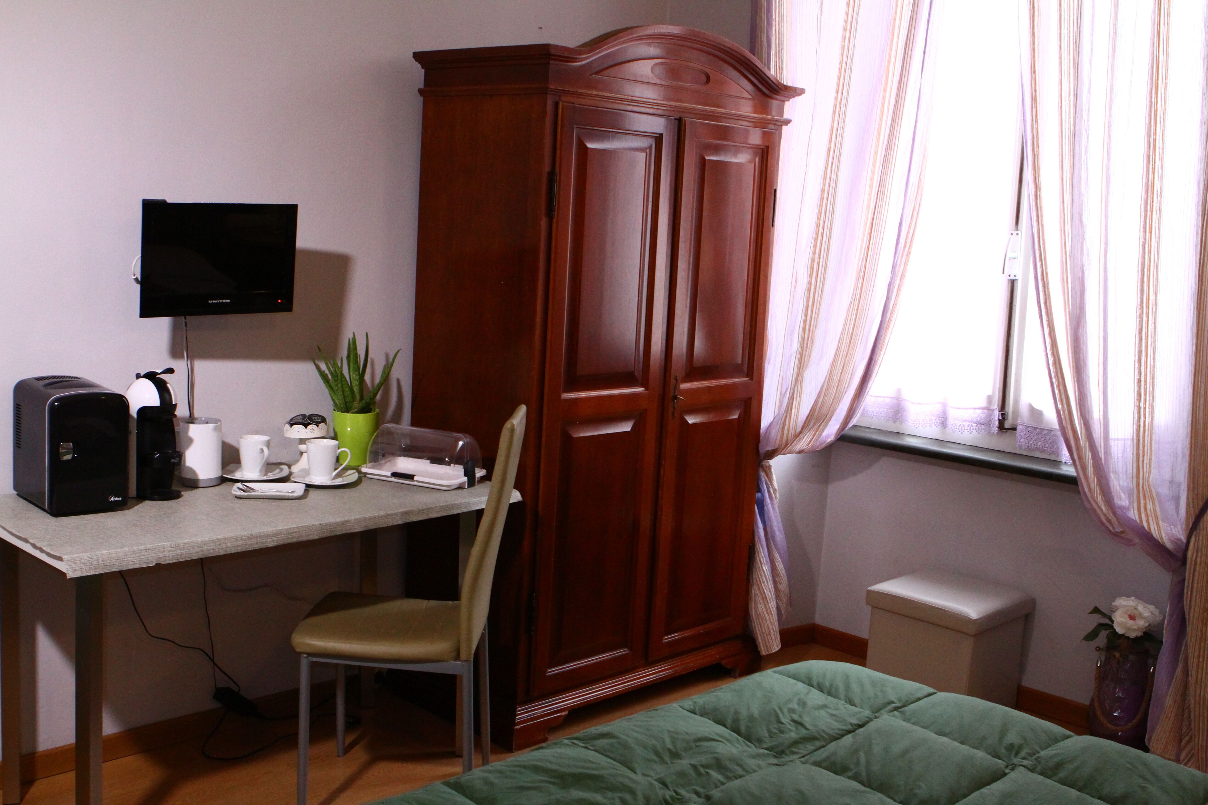 A room with a desk, chair, wardrobe, bed, TV, and a window with curtains.