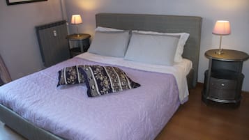 Siististi pedattu sänky, jossa on kuvioitu tyyny, kaksi yöpöytää, joissa on lamput, ja seinässä oleva patteri.