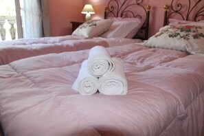 Un dormitorio con dos camas, cada una con ropa de cama rosa y almohadas estampadas. Hay toallas blancas enrolladas en la cama del primer plano.