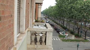 A street view with parked cars, a pedestrian crossing, and a row of trees.