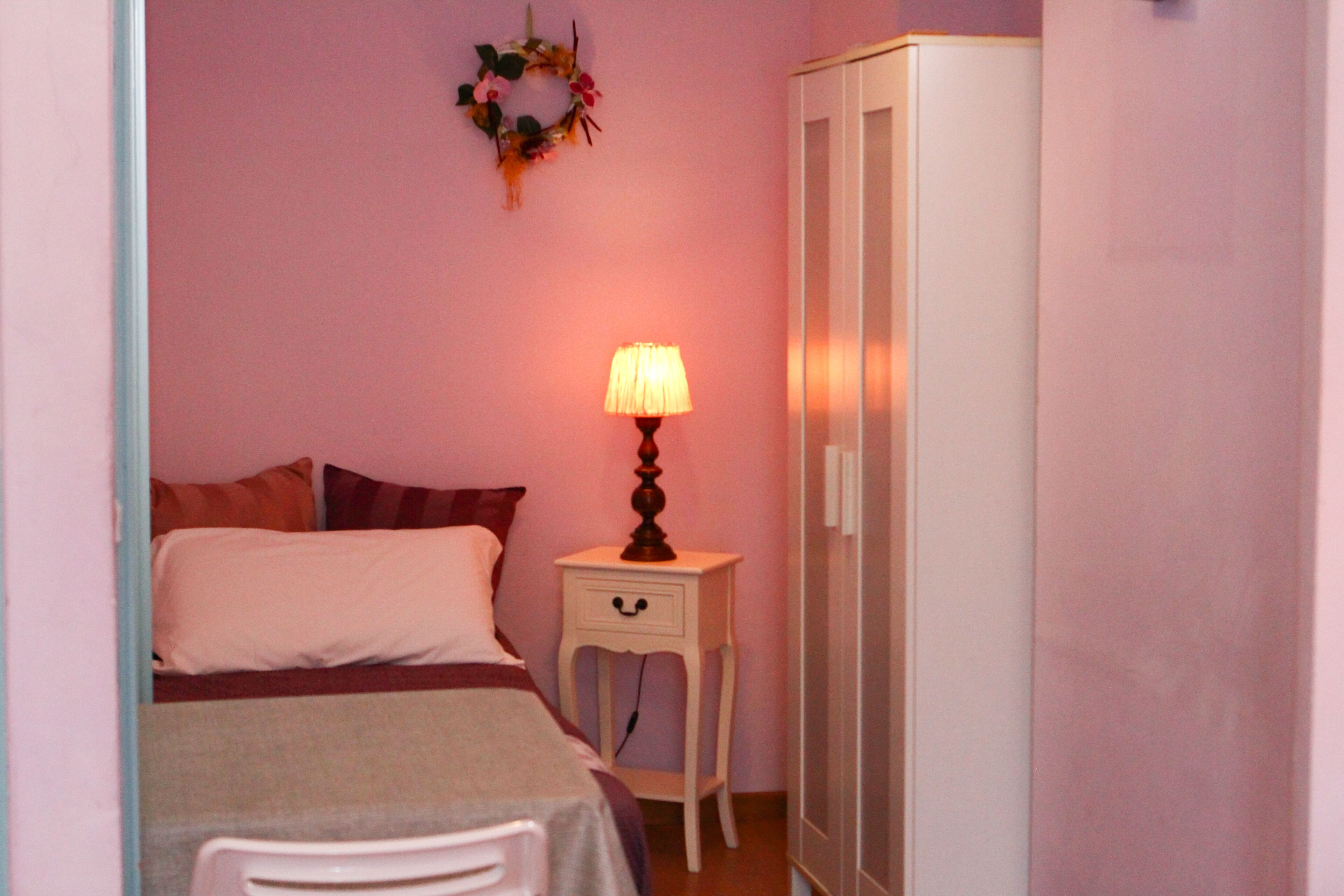 A bedroom with a bed, a bedside table with a lamp, a wardrobe, and a wall decoration.