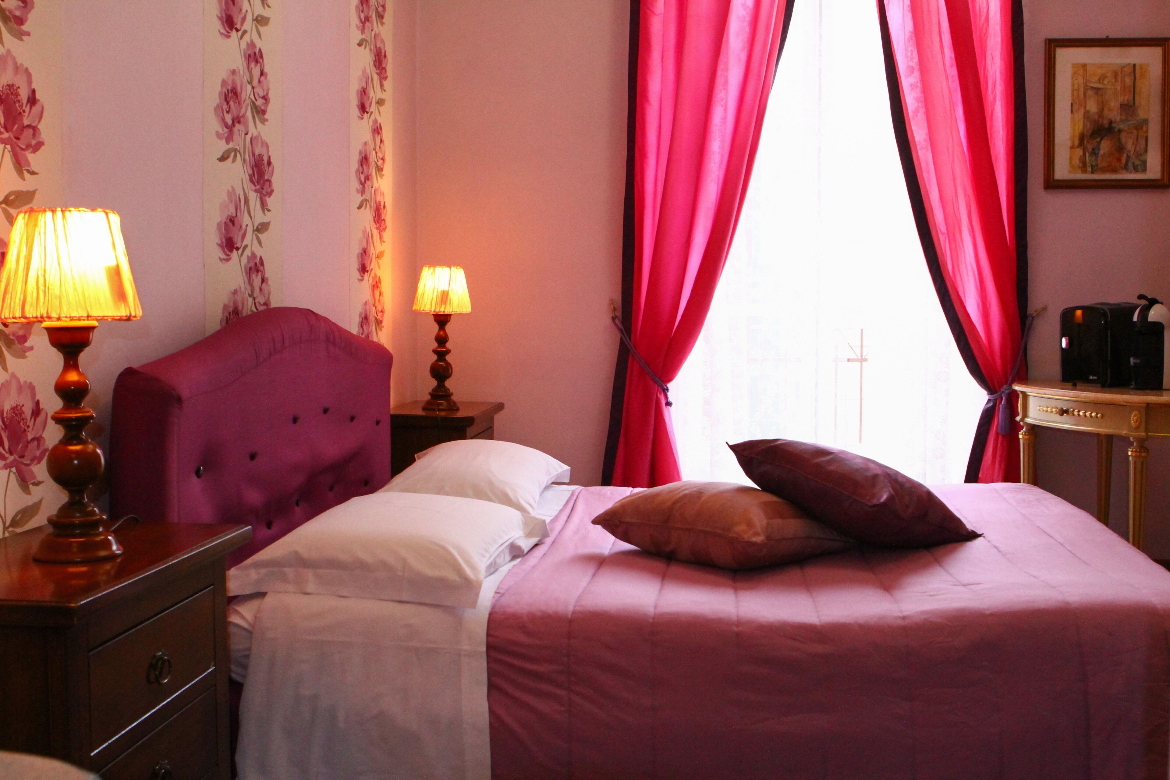 A hotel room with a bed, two bedside lamps, a nightstand, a dresser, and a coffee machine.