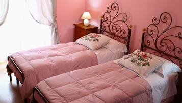 Quarto com duas camas, cada uma com colcha rosa e almofadas florais, uma mesa de cabeceira com abajur, e uma parede rosa.
