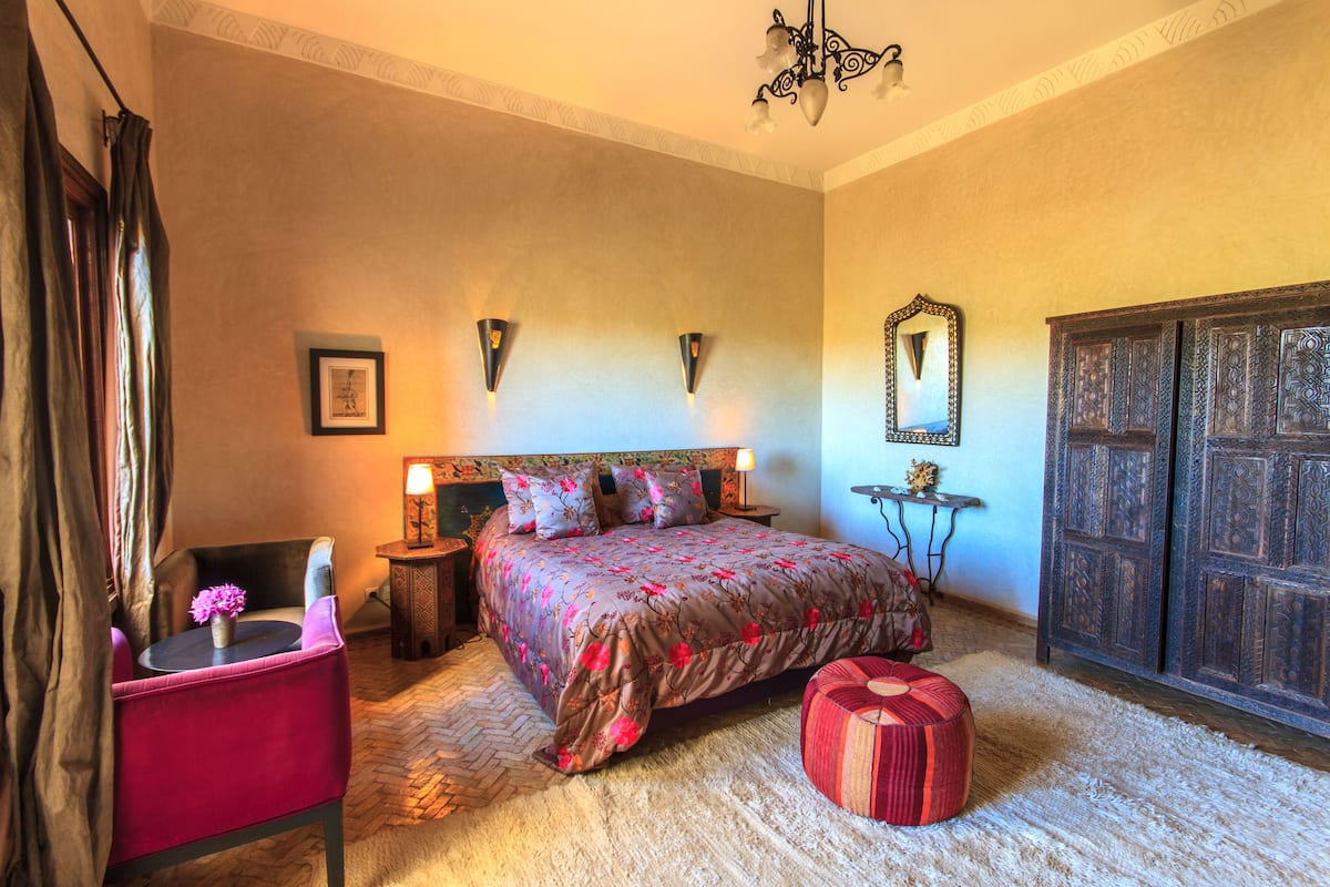 A bedroom with a bed, a chair, a nightstand, a mirror, and a wardrobe.