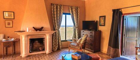 A room with a fireplace, a television, a bed, a chair, and a view of the outdoors.