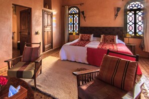 A traditional room with a large bed, two chairs, a small table, and a window with stained glass. - Kasbah Tabelkoukt (Mirleft)