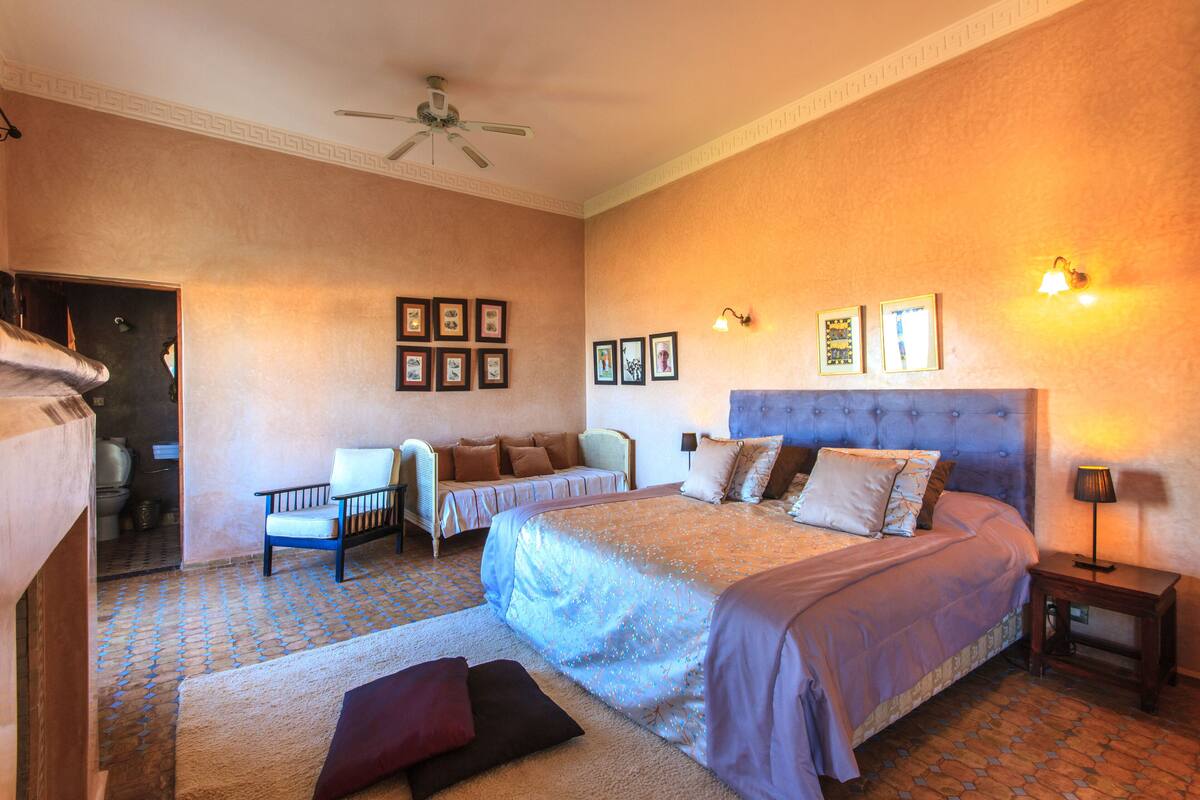 A bedroom with a large bed, a chair, a small table, and a ceiling fan.