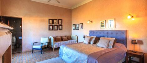 A bedroom with a large bed, a chair, a small table, and a ceiling fan.