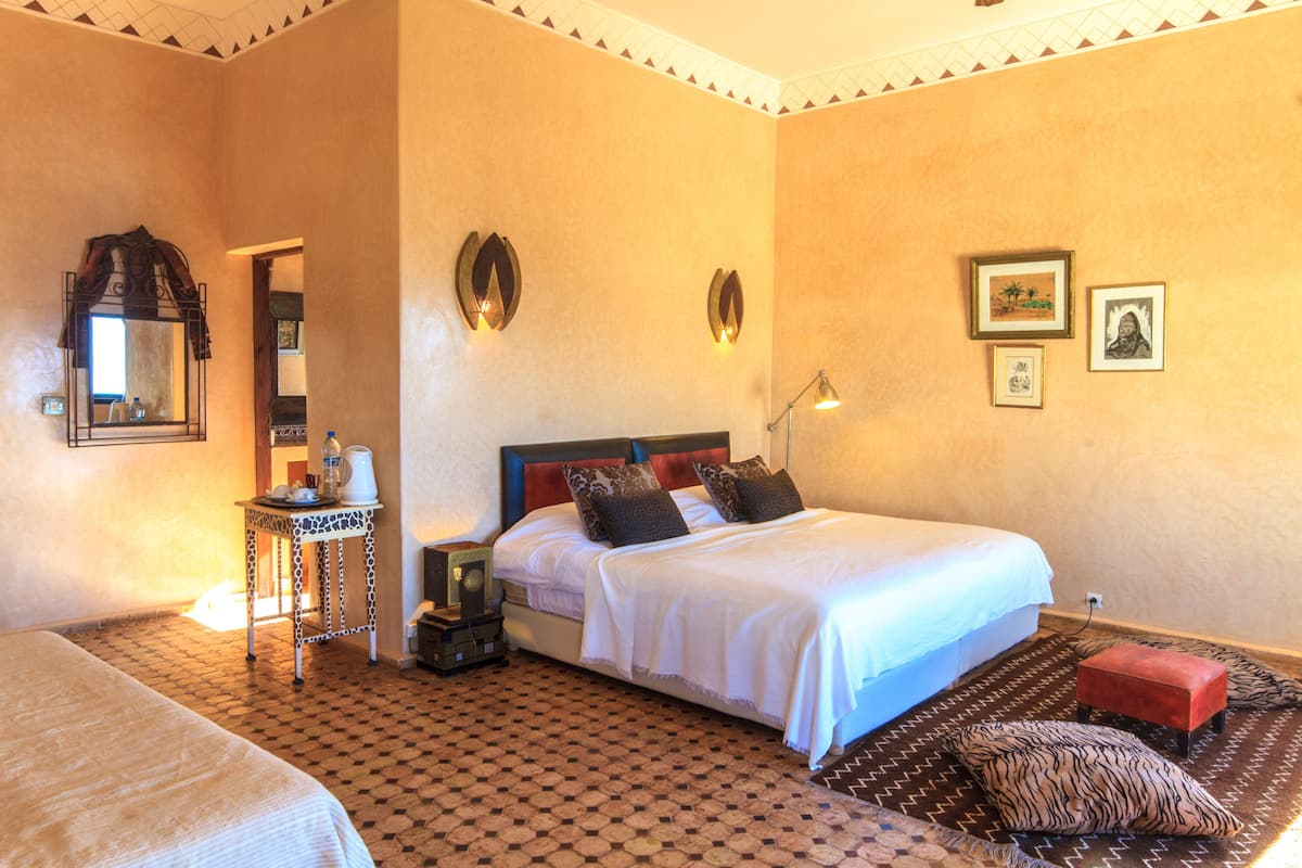 A hotel room with a large bed, a small table with a lamp, and a mirror.