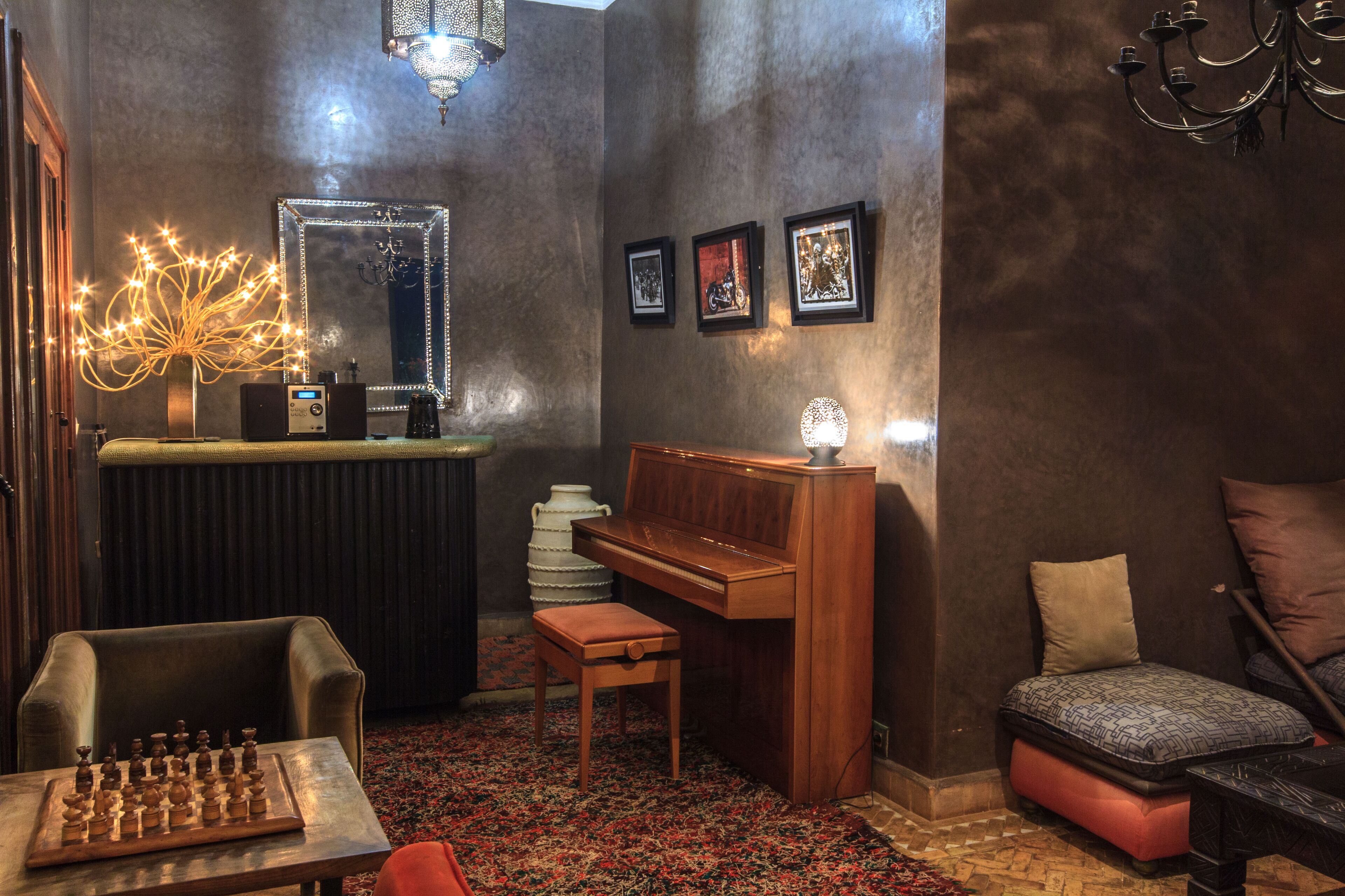 Una habitación acogedora con un piano, un tablero de ajedrez, un espejo y cuadros en la pared.