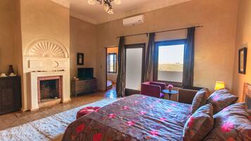 A bedroom with a large bed, a fireplace, a desk, and a view of the desert.