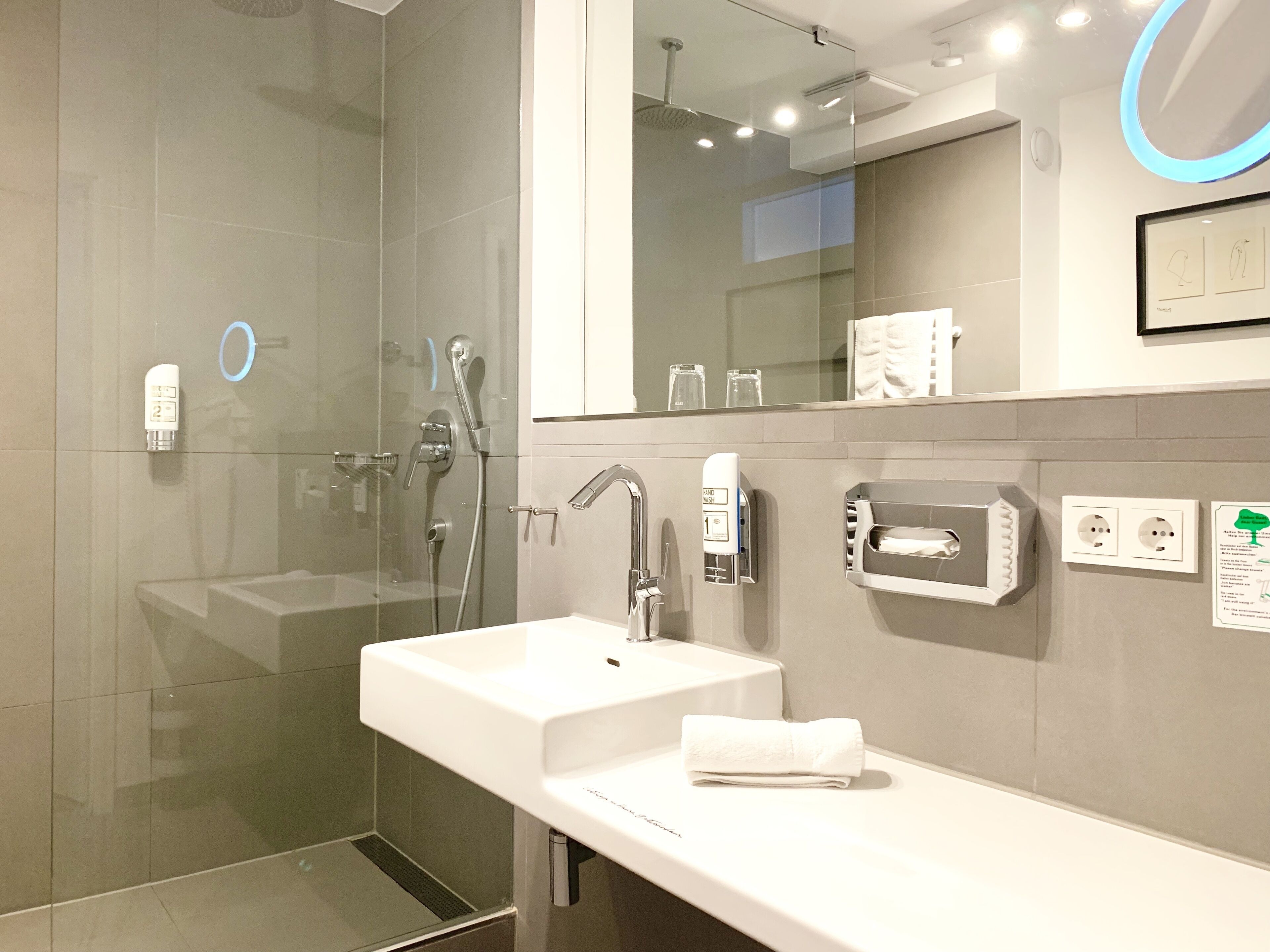 A modern bathroom with a glass shower enclosure, a white sink, and a large mirror.