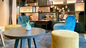 Una sala de estar moderna con una mesa redonda, dos sillones azules y una estantería con libros y adornos.