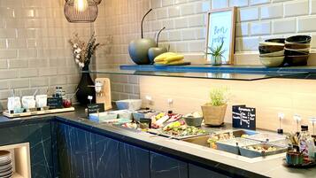 Zona de bufé con diversas opciones de comida, incluyendo platos veganos y caseros, y un letrero que dice "Bonjour Jour".