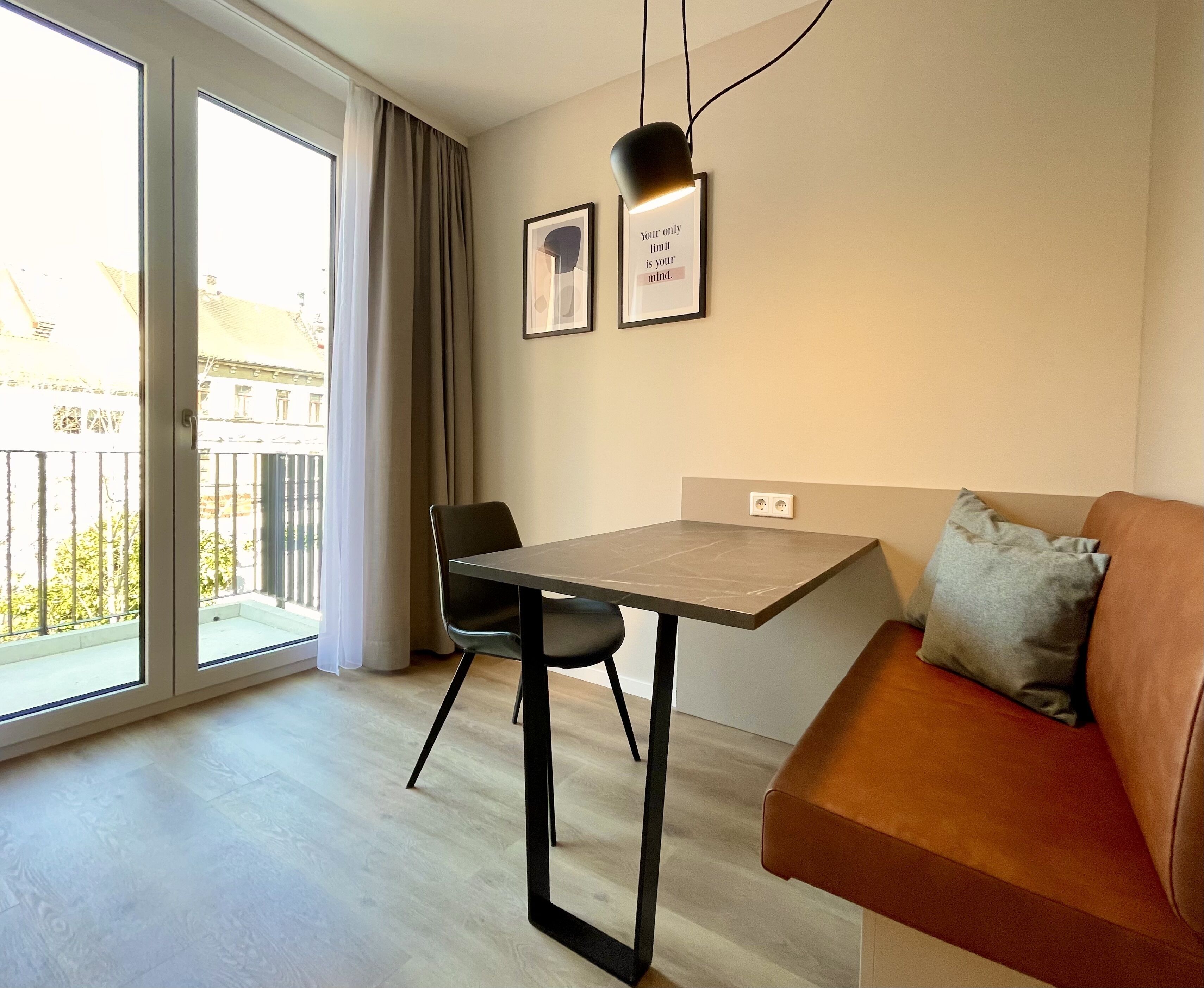 Una sala moderna con sofá, mesa de comedor y sillas. Tiene un balcón con vistas a edificios y árboles.