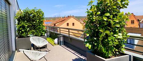 Una terraza en la azotea con una silla blanca, una planta en maceta y vistas a edificios al fondo.