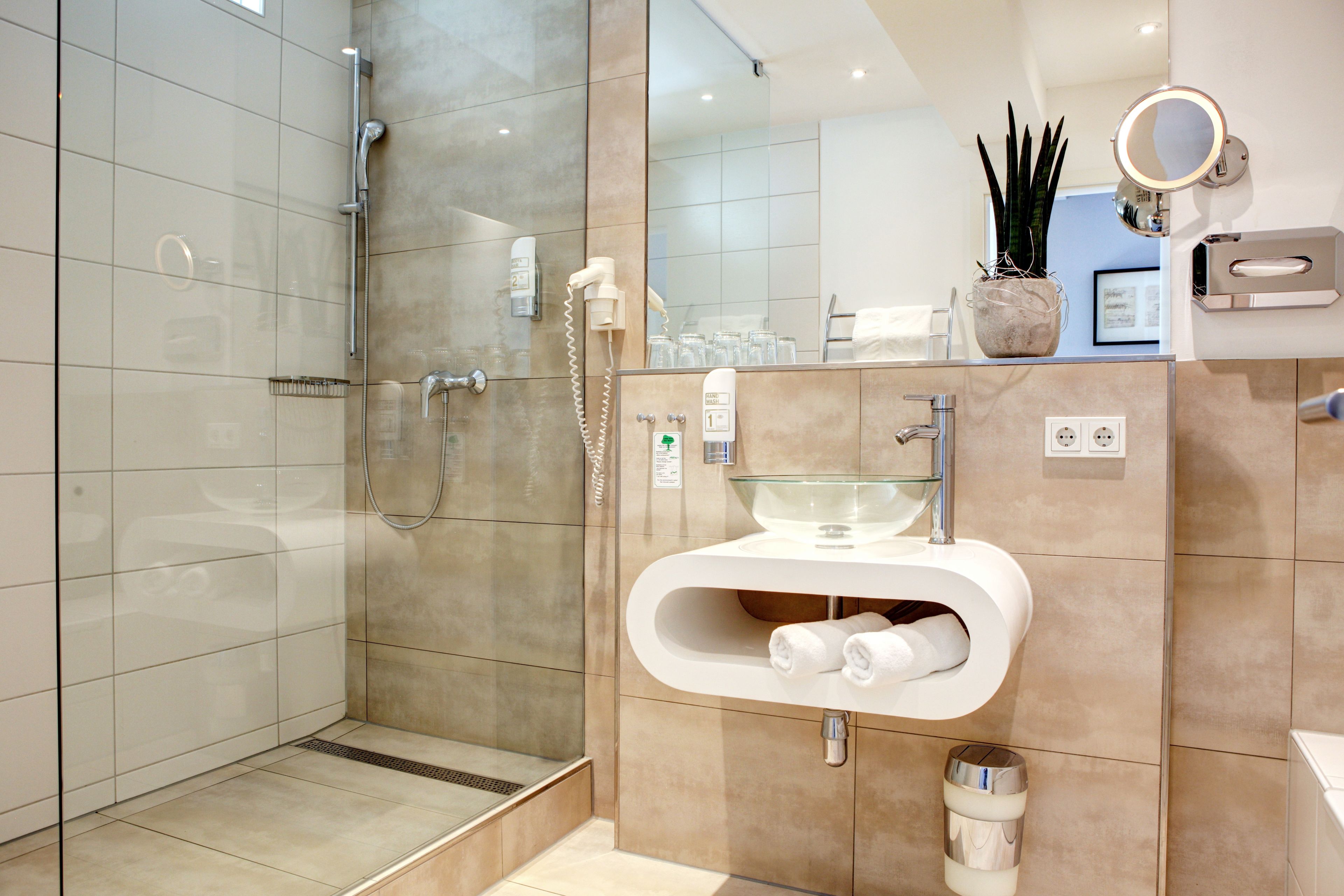 A modern bathroom with a glass shower enclosure, a glass sink, and a vanity with a mirror.