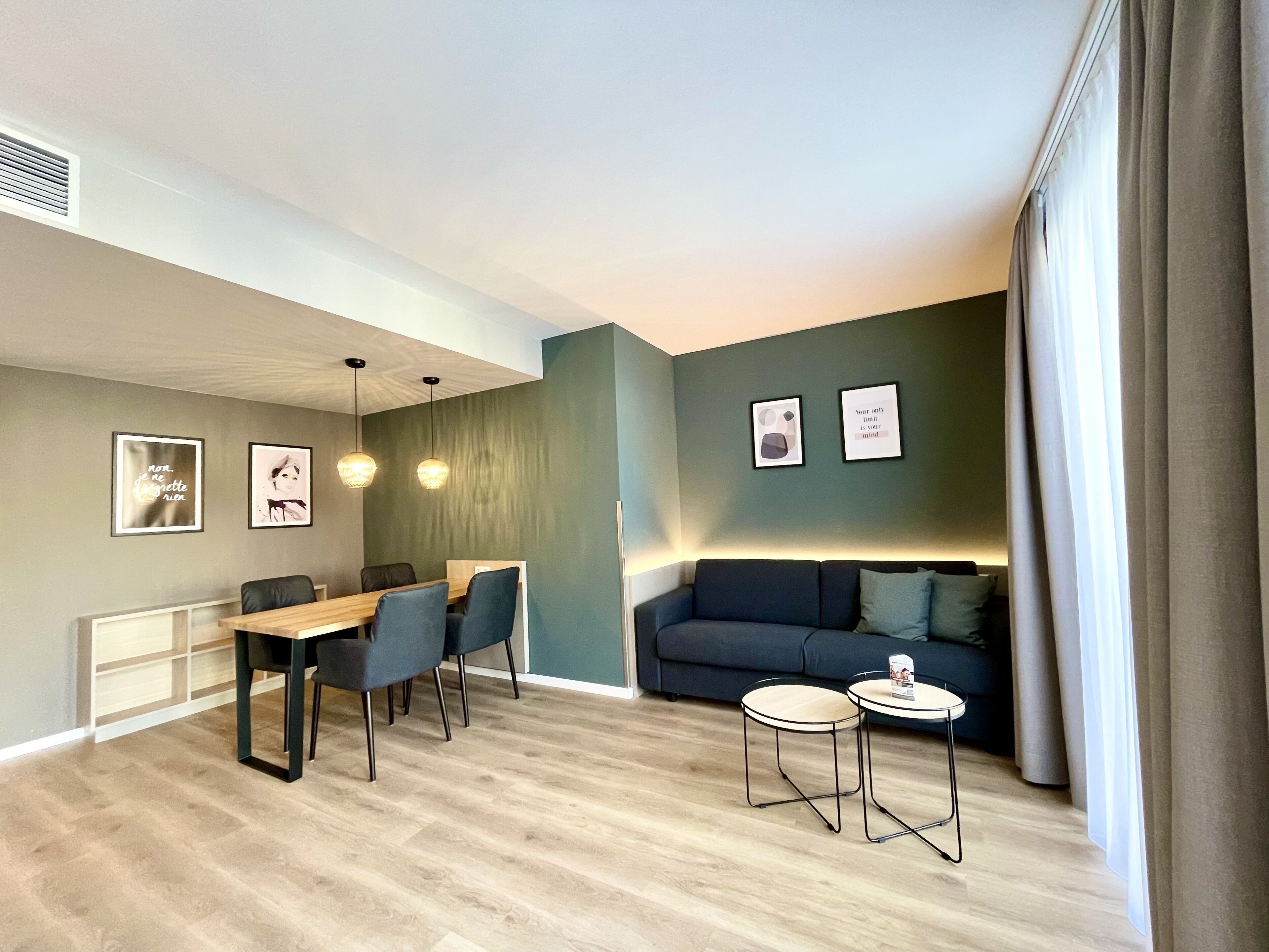 Una sala de estar moderna con comedor, un sofá, dos mesitas y obras de arte en las paredes.