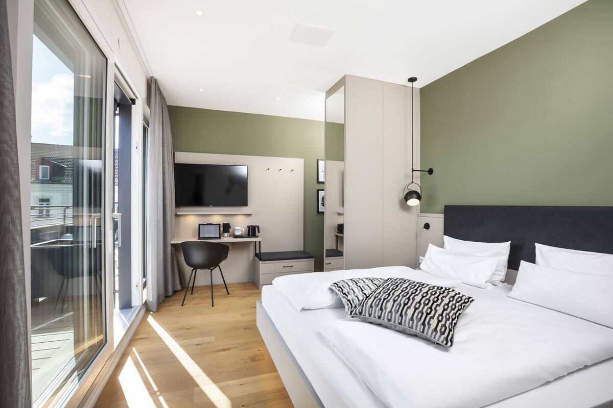 Een moderne hotelkamer met een groot bed, een bureau, een televisie en een balkon met een glazen deur.