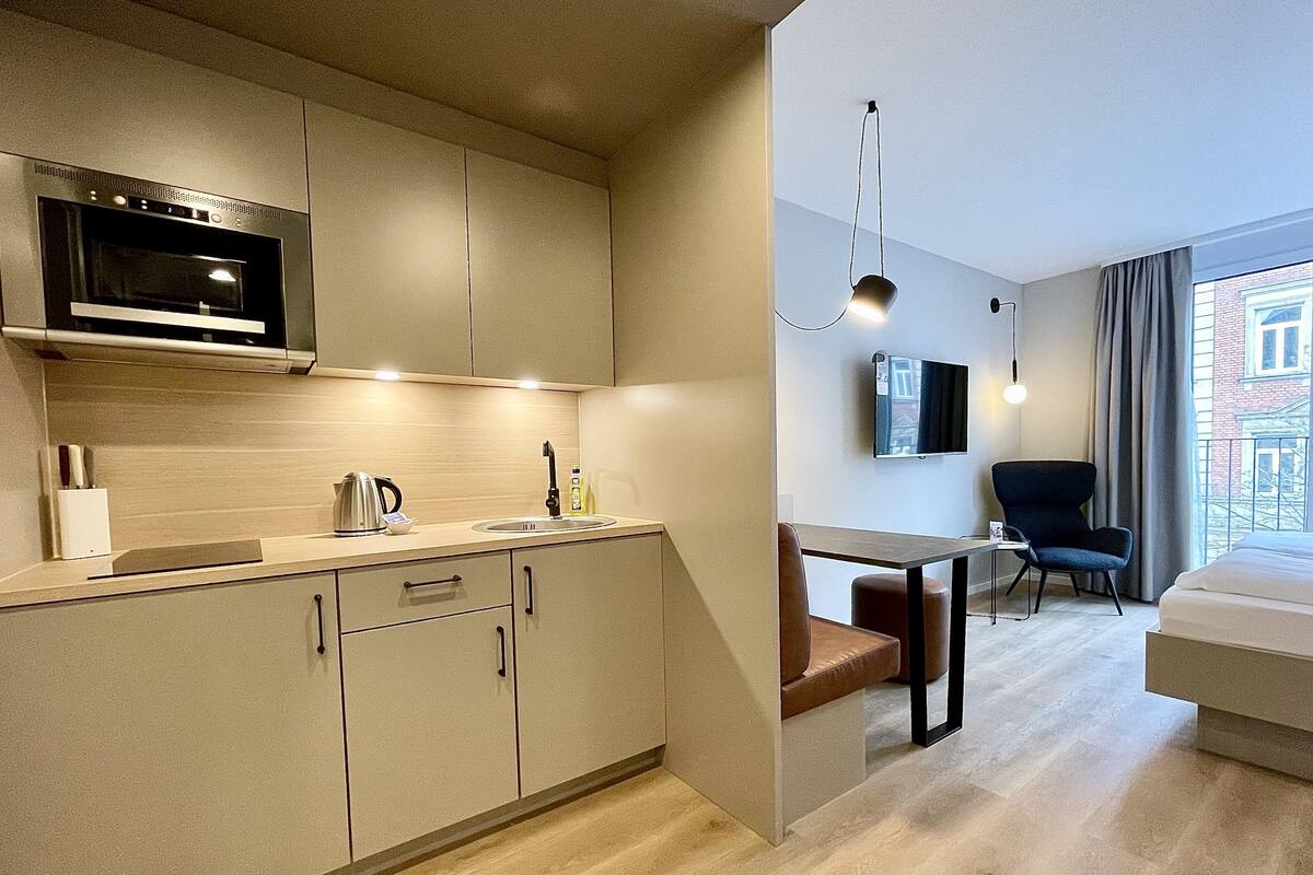 Een moderne keuken met een inbouwoven en magnetron, een eethoek met tafel en stoelen, en een groot raam met uitzicht op de stad.