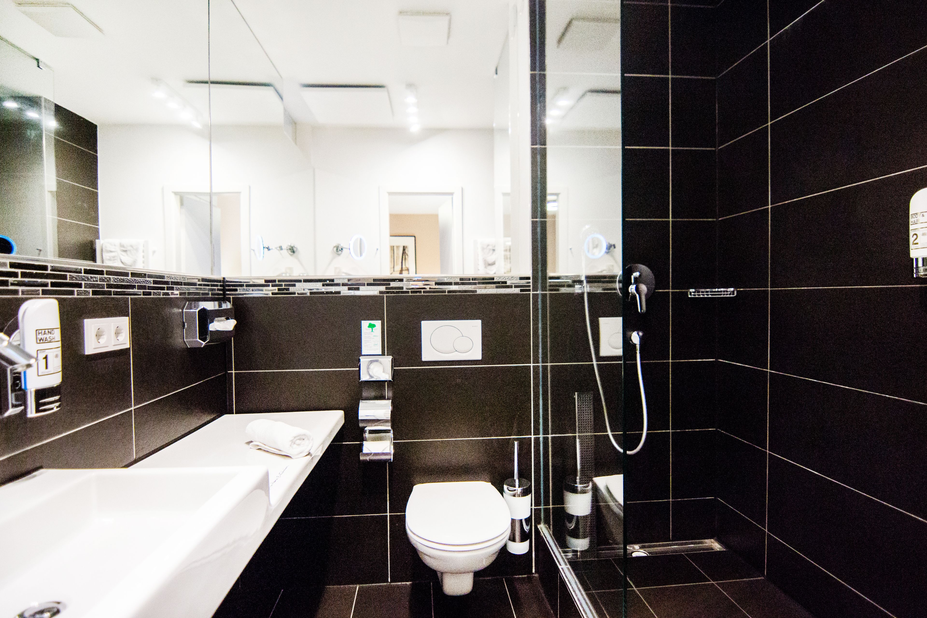 Un baño moderno con un espejo grande, un lavamanos blanco, un inodoro y una zona de ducha con paredes de vidrio.