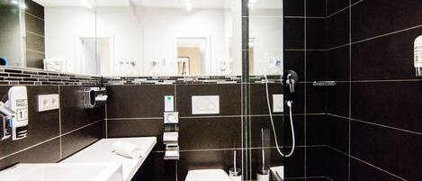 Un baño moderno con un espejo grande, un lavamanos blanco, un inodoro y una zona de ducha con paredes de vidrio.