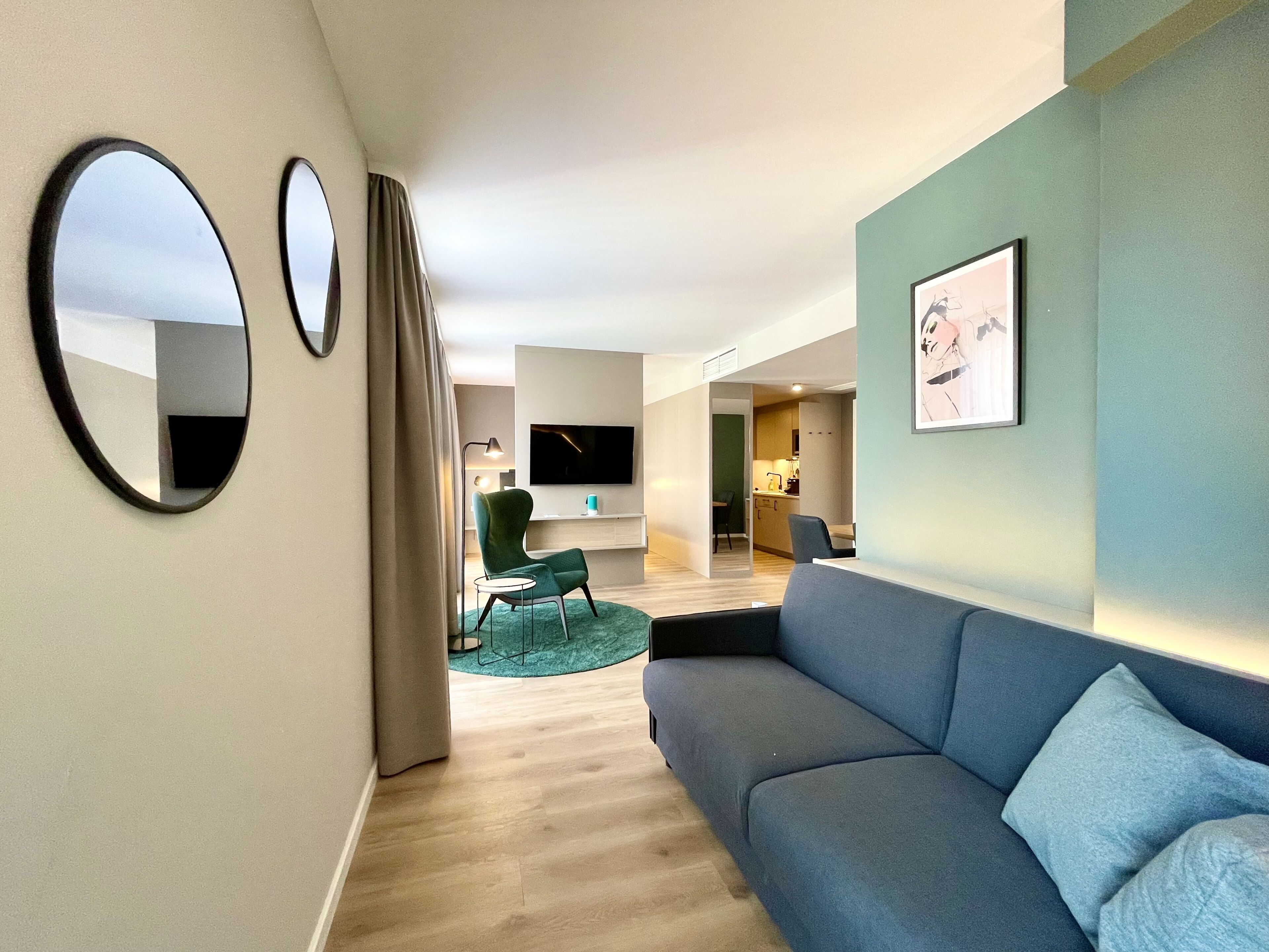 Una sala de estar moderna con un sofá gris, un espejo redondo y un televisor de pantalla plana.