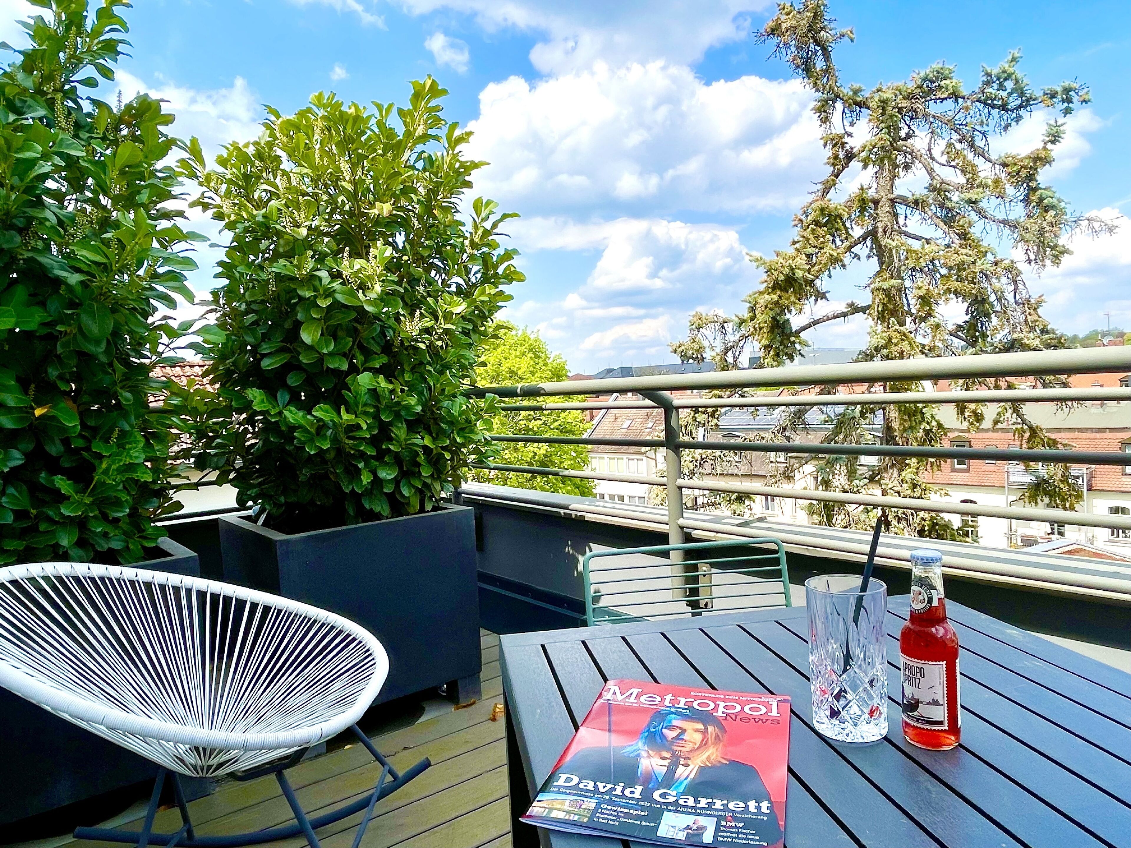 A balcony with a white chair, a magazine, a glass, and a bottle.