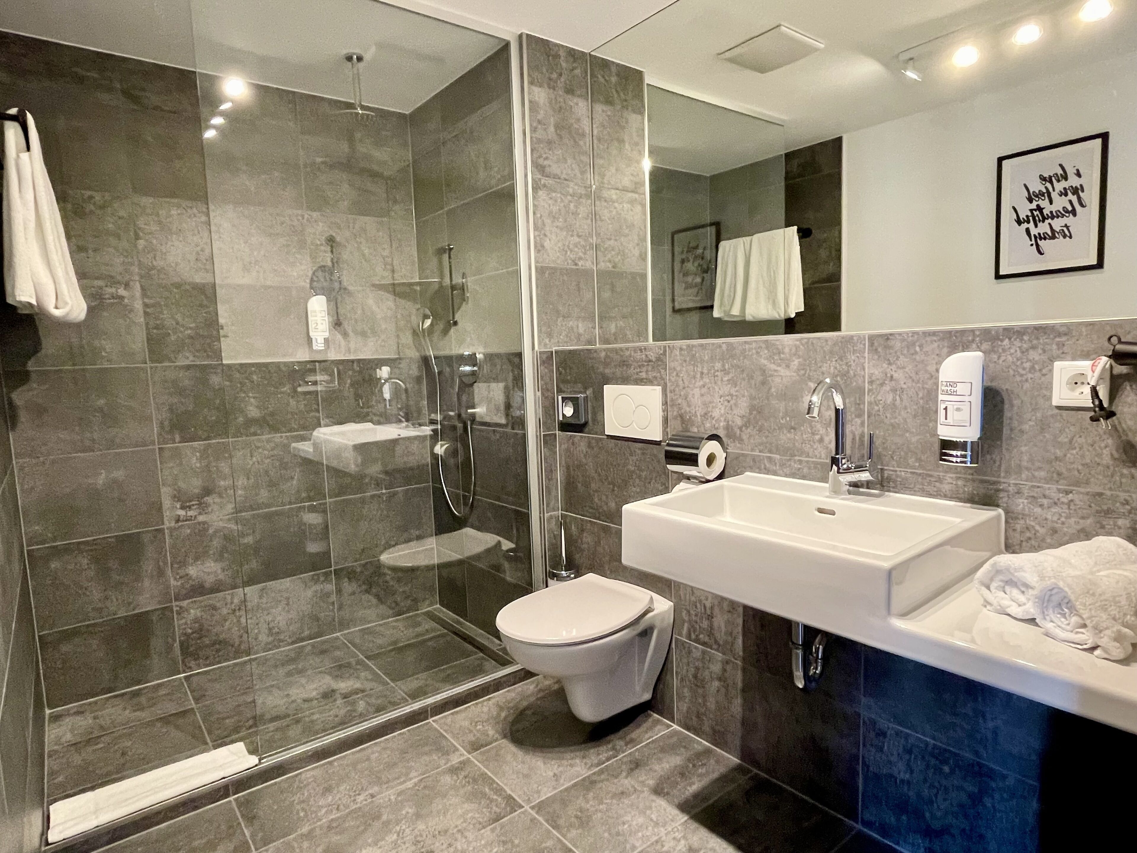 Un baño moderno con ducha de vidrio, lavamanos blanco y retrete.