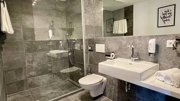 Un baño moderno con ducha de vidrio, lavamanos blanco y retrete.