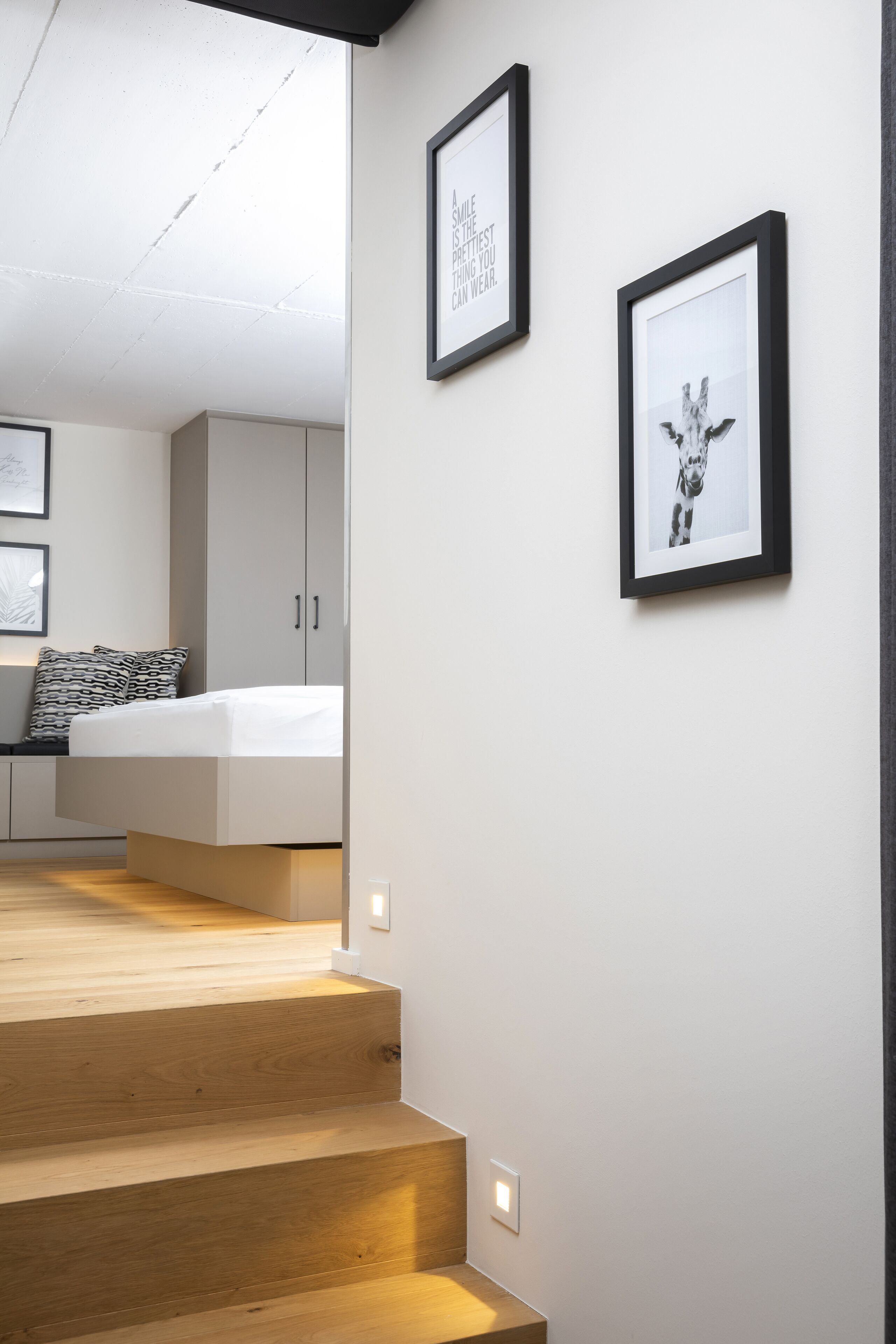 Una escalera lleva a un dormitorio con una cama, un armario y dos cuadros en la pared.