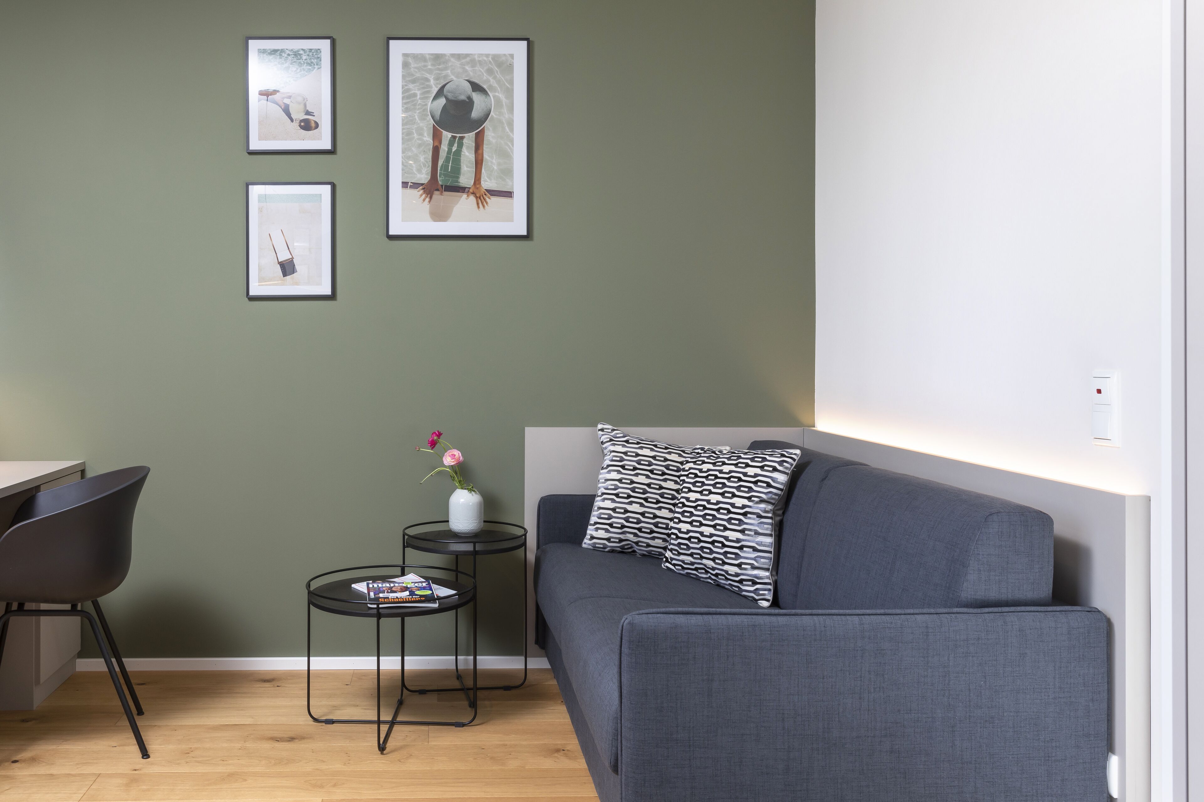 A modern living room with a grey sofa, a small round table with a vase of flowers, and framed artwork on the wall.