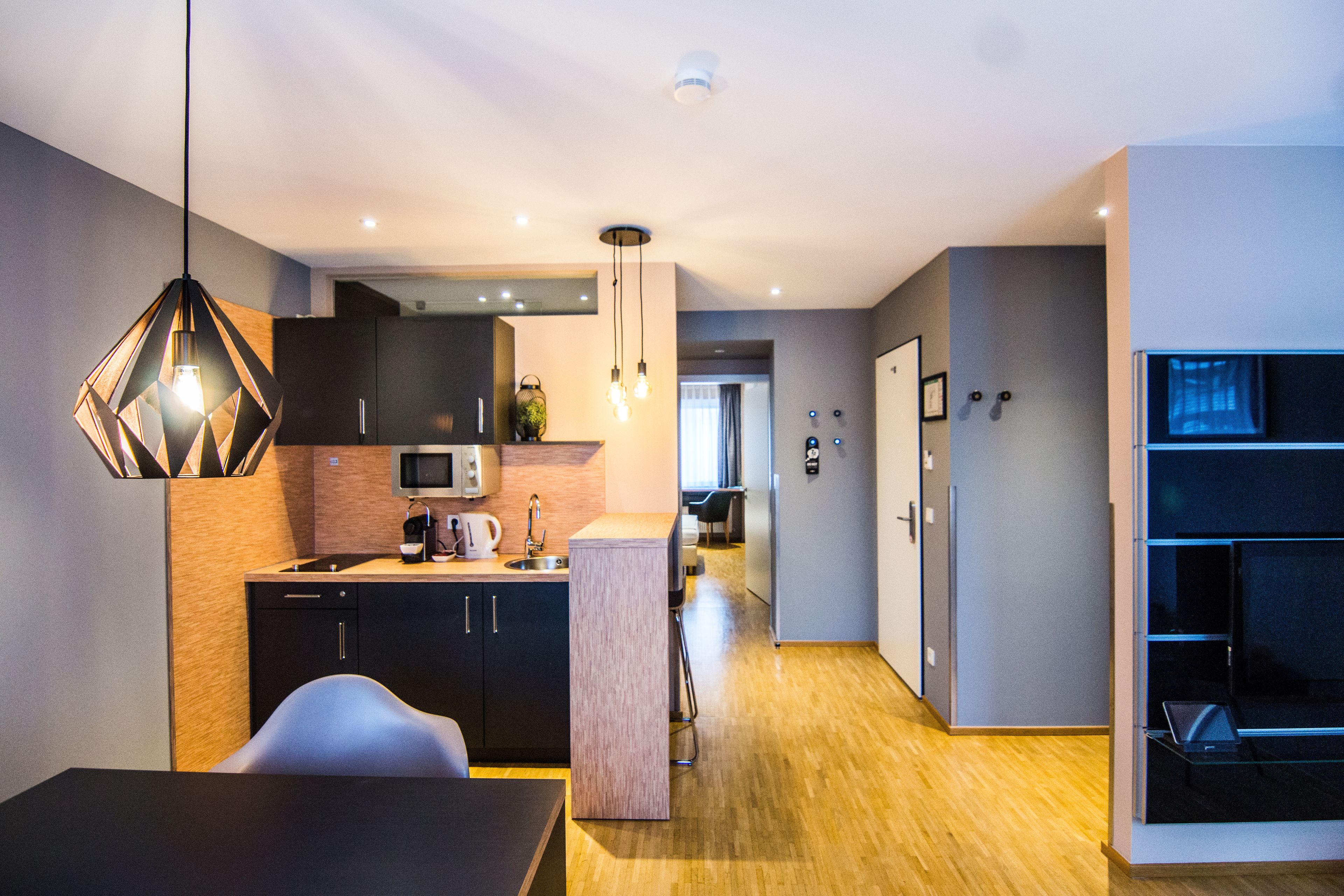 A modern kitchen with a dining area, wooden flooring, and contemporary lighting fixtures.