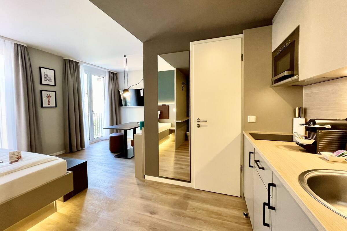Een moderne hotelkamer met kitchenette, eethoek en slaapkamer.
