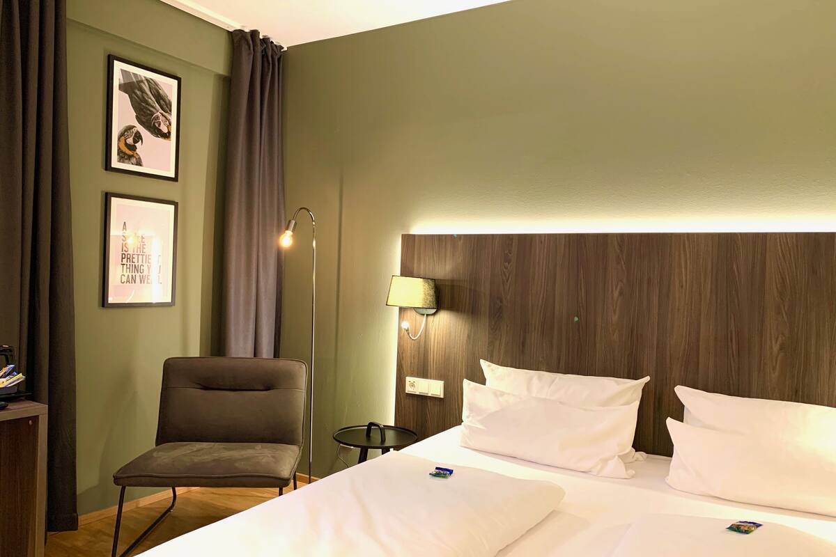 Een hotelkamer met een bed, een stoel, een nachtkastje en een wand met ingelijste foto's.