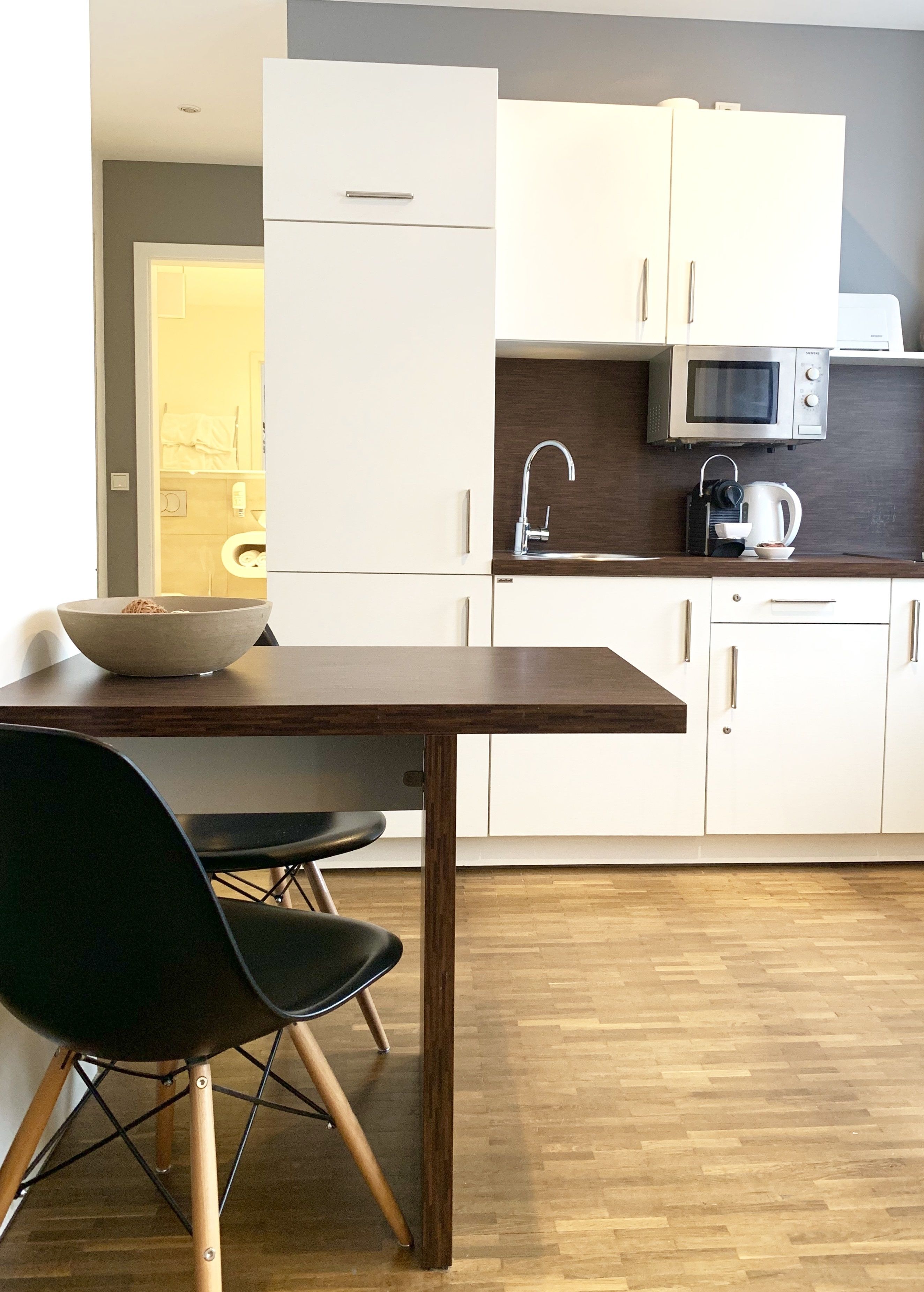 Una cocina moderna con armarios blancos, una mesa de comedor de madera y sillas negras.