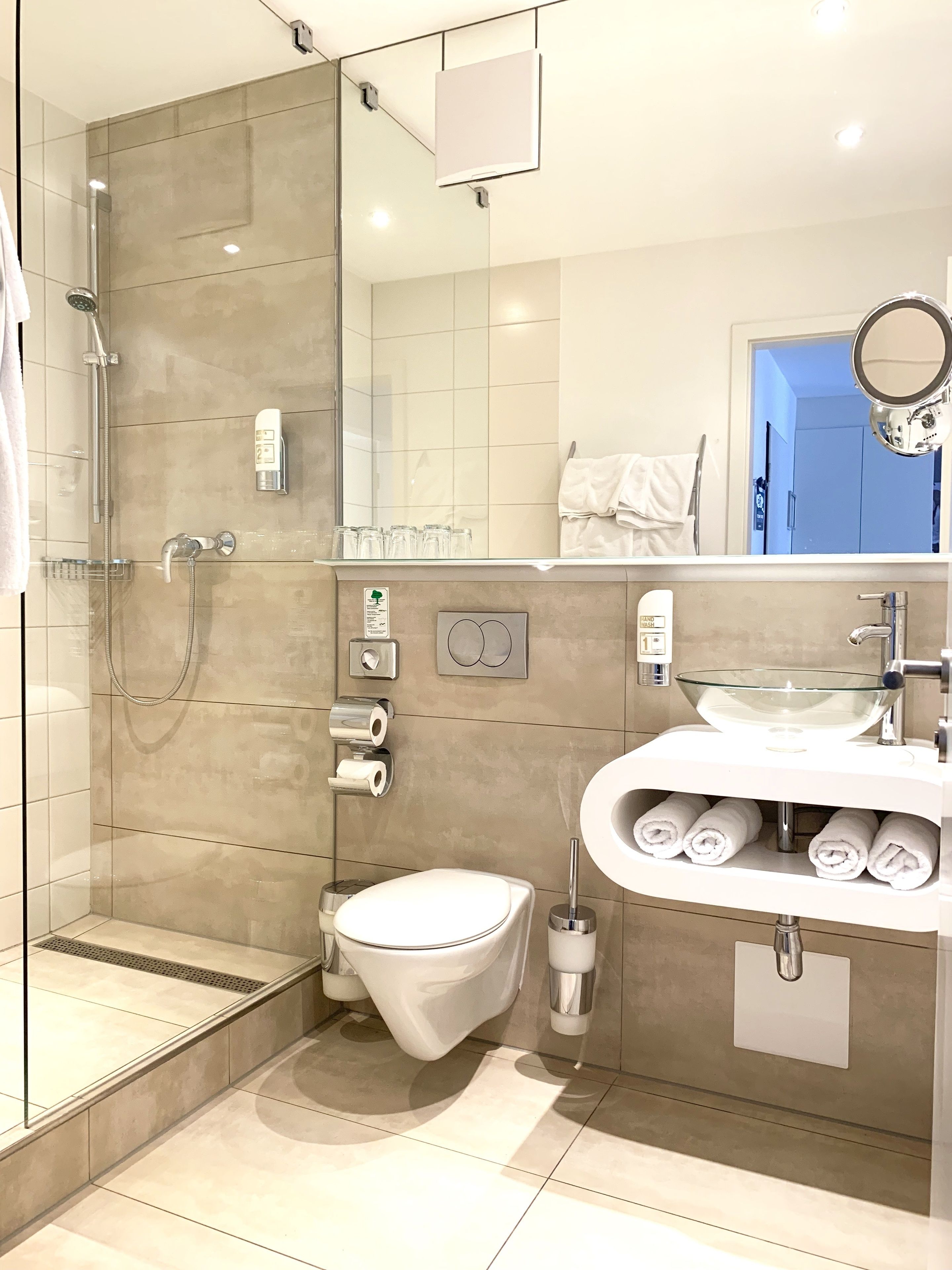 A modern bathroom with a glass-enclosed shower, a toilet, a sink with a glass bowl, and a mirror.