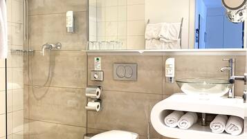 A modern bathroom with a glass-enclosed shower, a toilet, a sink with a glass bowl, and a mirror.