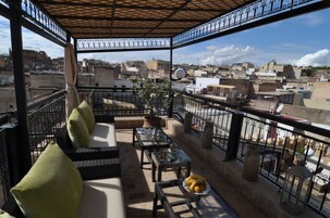Terraço no telhado com área de estar externa, uma mesa com uma cesta de frutas e vista para a cidade.