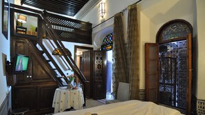 A hotel room with a bed, a small table with a lamp, a TV, a staircase, and a decorative door. - Riad Adarissa (Fes)