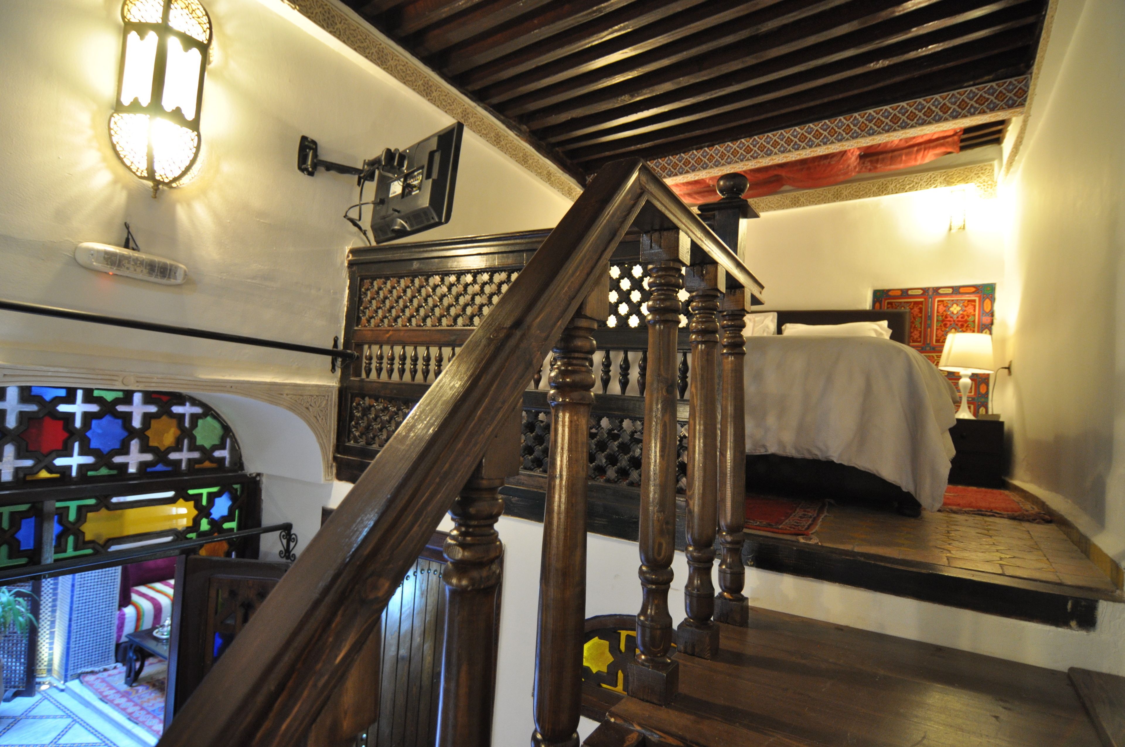 A bedroom with a bed, a nightstand, a lamp, and a wooden staircase.