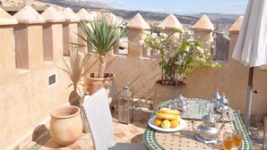 A terrace with a table set for a meal, potted plants, and a view of the city. - Riad Adarissa (Fes)