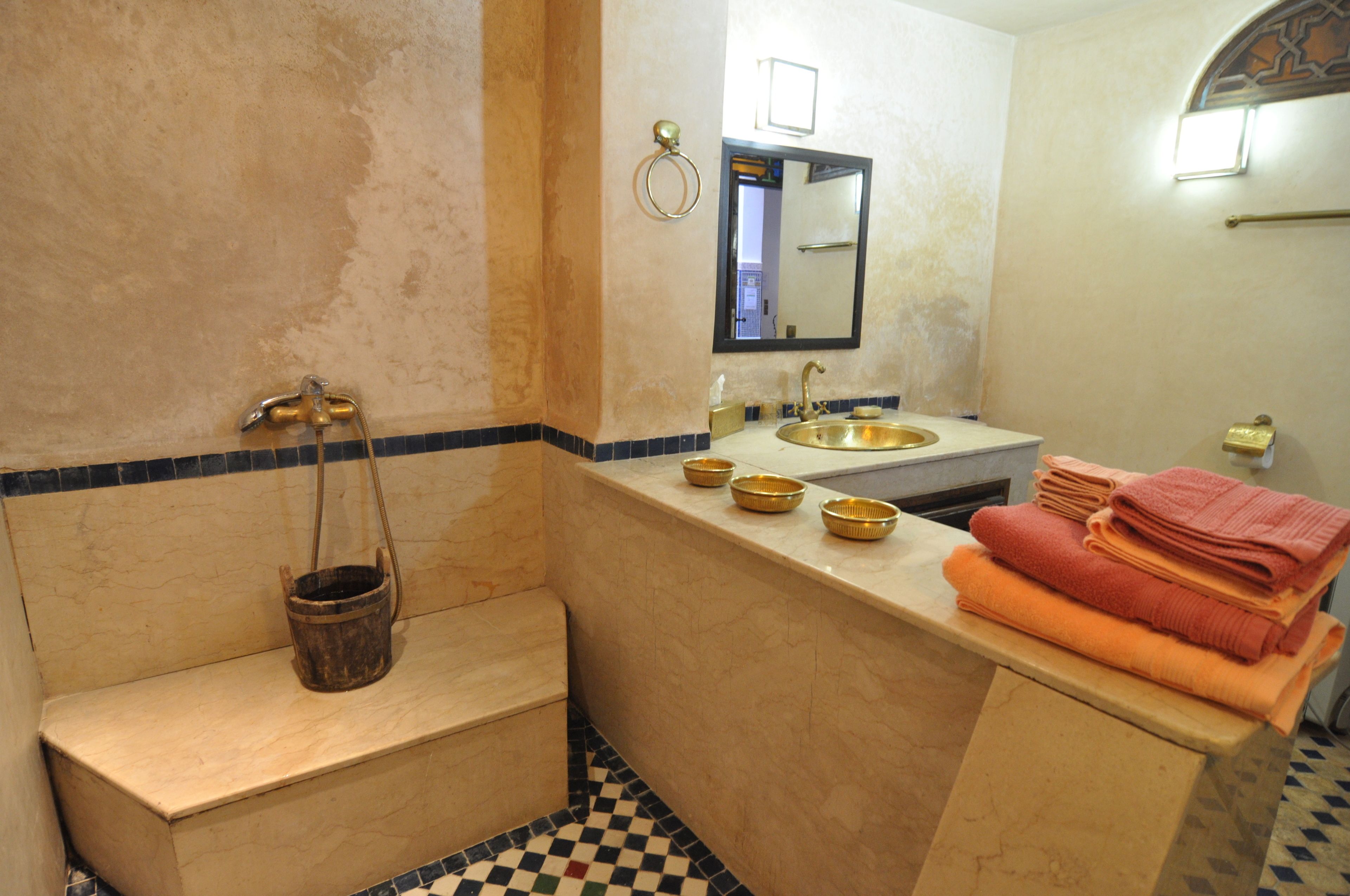Un baño con lavabo, espejo y una banca. Hay toallas apiladas en la encimera.